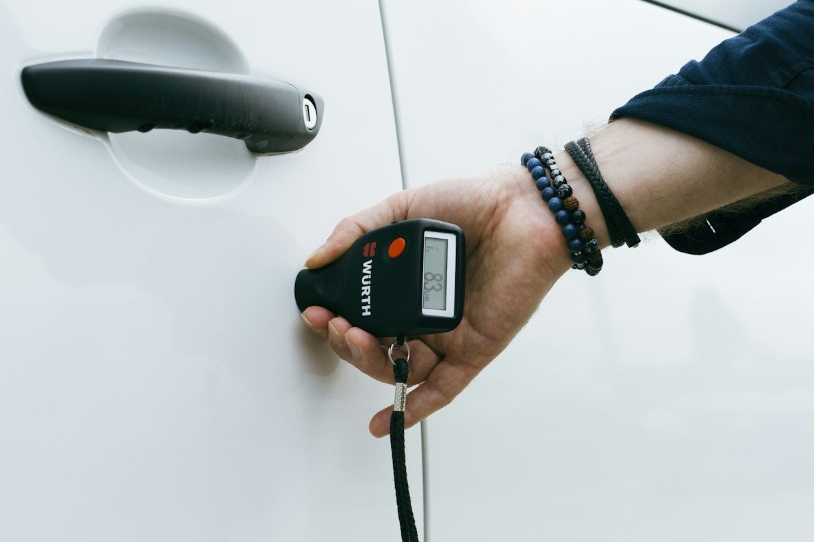 Hand misst die Lackdicke eines Autos an der Tür eines Gebrauchtwagens